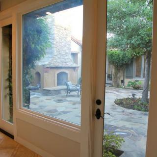 View of a charming courtyard with outdoor seating and stone flooring through a large window.