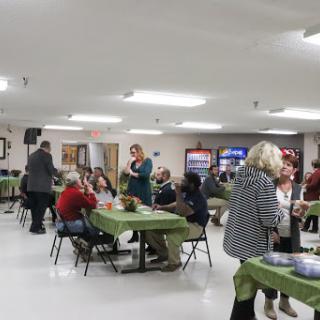 A community gathering taking place indoors, with people engaged in conversation and activities at tables.