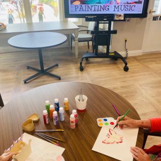 Senior residents engaging in a painting activity with music accompaniment.