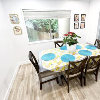 A bright and inviting dining area featuring a table adorned with a colorful tablecloth, surrounded by wooden chairs and a view of greenery outside.
