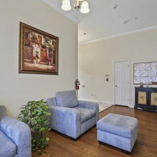 A cozy living room with armchairs, an ottoman, artwork on the wall, and a potted plant.