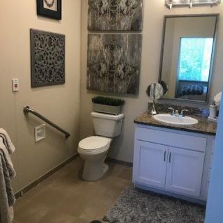 A well-decorated bathroom with a toilet, sink, and mirror, featuring wall decor and safety handrails.