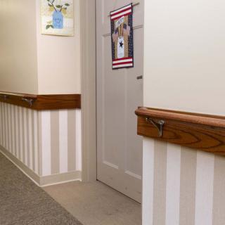 A hallway with striped walls, featuring a door adorned with artwork and wooden handrails.