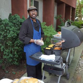 A chef grilling food outdoors at a barbecue setup.