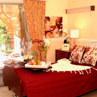 A cozy bedroom with red bedding and elegant decor, featuring a lamp and indoor plants.
