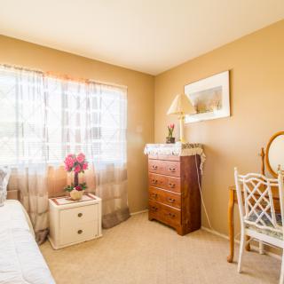 A cozy bedroom with natural light streaming through a window, featuring a dresser, chair, and decor.