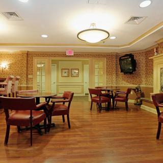 A well-lit dining area with wooden tables and chairs, featuring elegant decor and a mounted television.