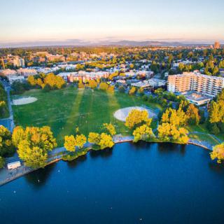 A scenic aerial view of a park with a lake, surrounded by urban buildings and greenery.