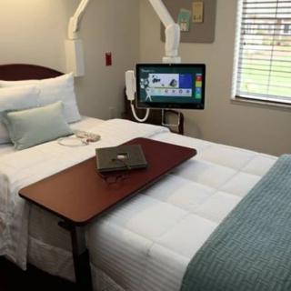 A hospital room with a bed, adjustable tray table, and wall-mounted television.