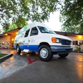 A white and blue van parked in a lot next to a building, surrounded by trees.