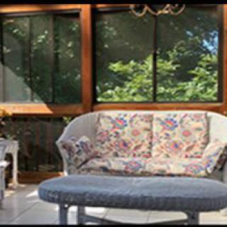 A sunlit conservatory featuring a floral-patterned sofa with matching cushions and a round table.