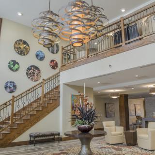 A modern lobby interior featuring a grand staircase, unique chandelier, and decorative wall artwork.