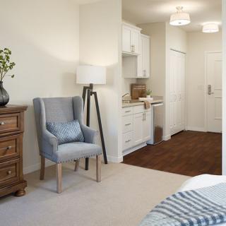 A cozy bedroom interior with a chair, dresser, and a kitchenette in a modern design.