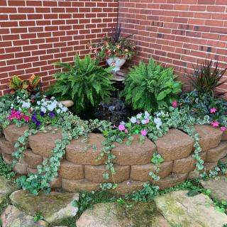 A small garden with colorful flowers and lush plants against a brick wall.