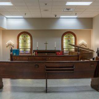 Interior of a religious space featuring a wooden altar and stained glass windows.