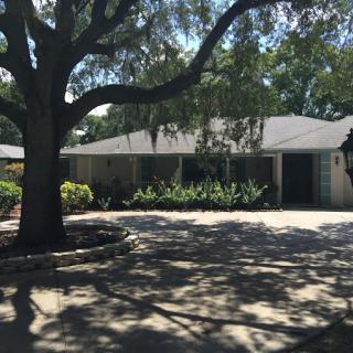 A single-story house with a large tree casting shadows on the driveway.