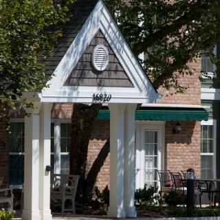 A building entrance featuring an awning and porch, surrounded by trees.