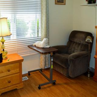 A cozy living room with a reclining chair, table, and a cat by the window.