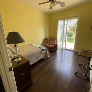 A cozy bedroom featuring a bed, an armchair, a desk, and large sliding doors leading to the outdoors.
