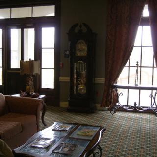 A cozy living room featuring a vintage clock, comfortable seating, and large windows.