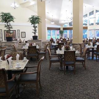 A spacious and elegantly decorated dining area with tables and chairs, featuring large windows and potted plants.