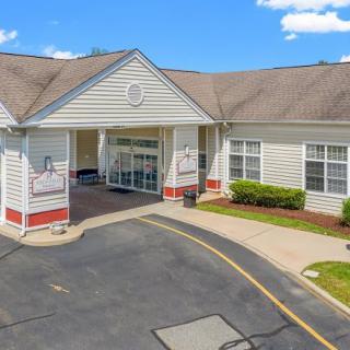 The image shows the entrance of a building with a driveway and parking area.