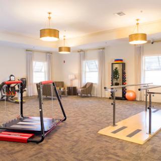 A well-lit rehabilitation and fitness space featuring exercise equipment such as a treadmill and parallel bars.