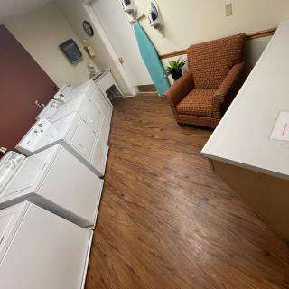 A cozy laundry room featuring washing machines, a dryer, an ironing board, and a comfortable chair.