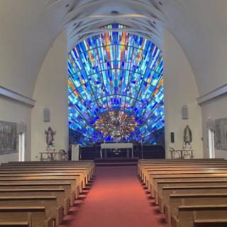 Interior view of a church featuring a vibrant stained glass window behind the altar.