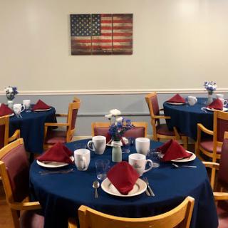 A beautifully arranged dining area featuring tables set with red napkins and coffee mugs, adorned with an American flag artwork.