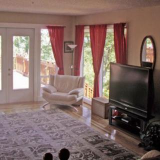 A cozy living room featuring a large television, comfortable chair, and bright red curtains allowing natural light to filter in.