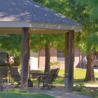 A serene outdoor gazebo with patio furniture surrounded by lush trees.