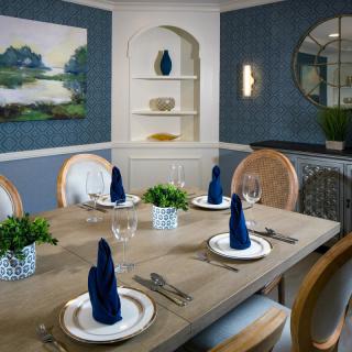 A stylish dining room featuring a neatly set table with blue napkins, elegant decor, and wall artwork.