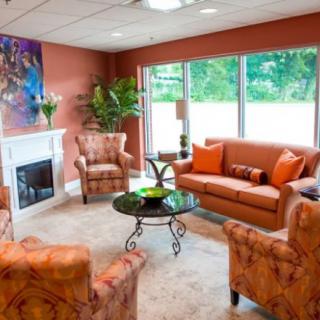 A cozy living room featuring orange sofas and chairs, a fireplace, and large windows providing natural light.