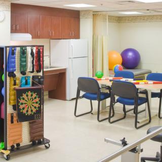 A therapy room equipped with exercise and rehabilitation tools, including a dartboard and colorful exercise balls.