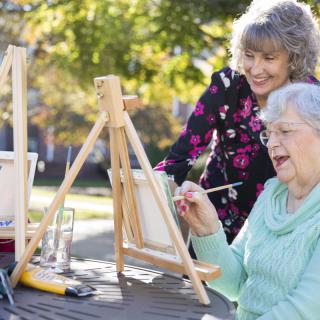 Elderly women enjoying a painting session outdoors on a sunny day.