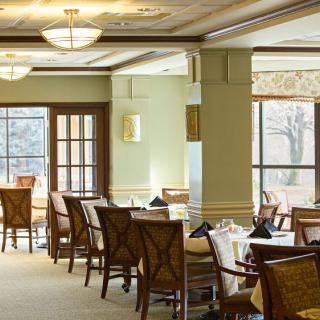 A well-lit dining area in a restaurant featuring multiple tables and chairs, with large windows allowing natural light to fill the space.
