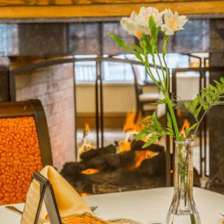 A cozy restaurant table setting with flowers and a fireplace in the background.