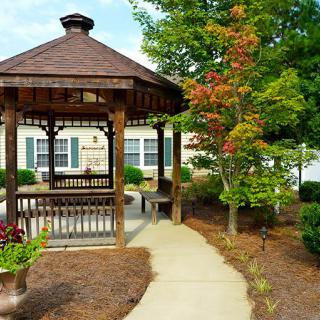 A wooden gazebo surrounded by a landscaped garden with a tree showing autumn colors.