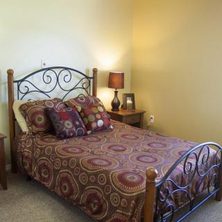 A cozy bedroom featuring a patterned bedspread and decorative pillows, with a lamp and picture frame on the bedside table.