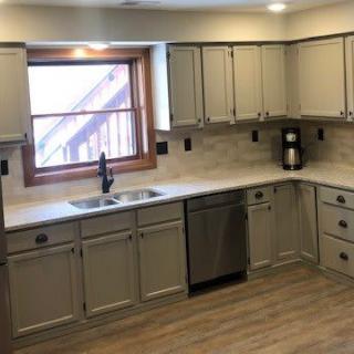 A modern kitchen with light-colored cabinets, a large window, and wood flooring.