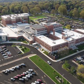 An aerial view of a modern institutional building surrounded by a large parking lot and green landscape.