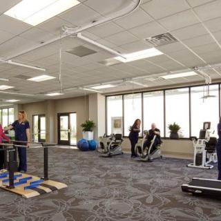 A physical therapy center with exercise equipment and people working out.