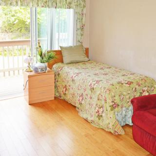 A cozy bedroom with a single bed featuring floral bedding, a side table, and natural light coming through a sliding door.