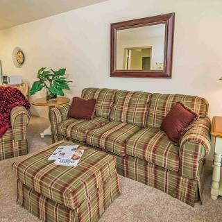 A cozy living room featuring a plaid-patterned sofa and armchair, complemented by a matching ottoman. The space is decorated with an indoor plant, a wall mirror, and decorative pillows on the furniture.