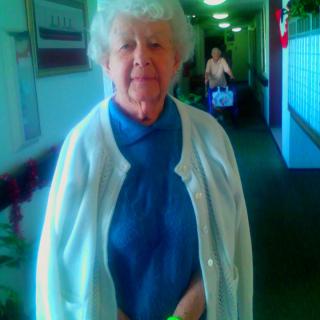 An elderly woman standing in a brightly lit hallway.
