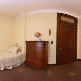 A cozy bedroom featuring a single bed, a wooden dresser, and an ornate door.