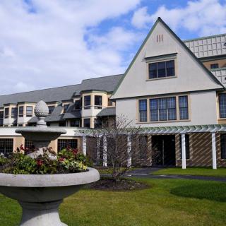 A large, modern building with a green lawn and decorative fountain under a partly cloudy sky.