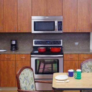A kitchen with wooden cabinets, a stove, and a microwave, featuring a dining table set with cups.