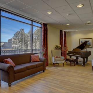 A cozy living room with a grand piano, comfortable seating, and large windows offering a scenic view.